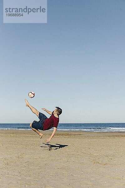 Kerl spielt Fußball am Strand