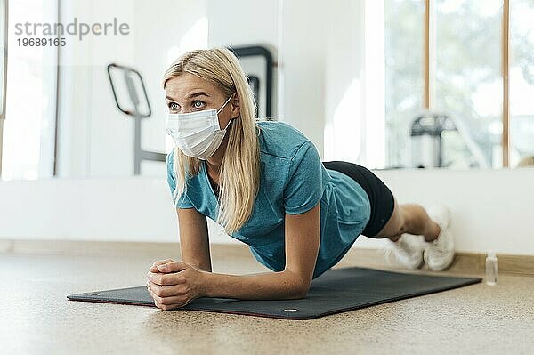 Seitenansicht einer Frau  die in einem Fitnessstudio mit medizinischer Maske während einer Pandemie trainiert