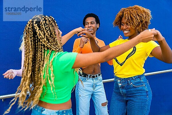 Dynamisches Foto von glücklichen multirassischen Freunden  die im Freien zusammen tanzen und sich an den Händen halten