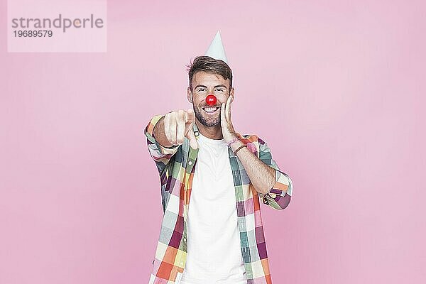 Junger Mann mit Clownsnase zeigt mit dem Finger auf rosa Hintergrund
