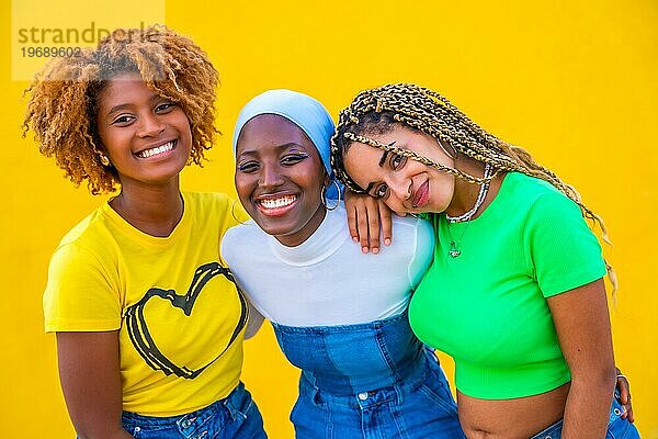 Close up Porträt von drei Frauen verschiedener Ethnien  die in die Kamera lächeln  vor einem gelben Hintergrund