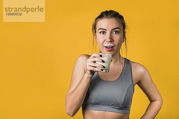 Erstaunte attraktive junge Frau Sportkleidung mit Glas Milch