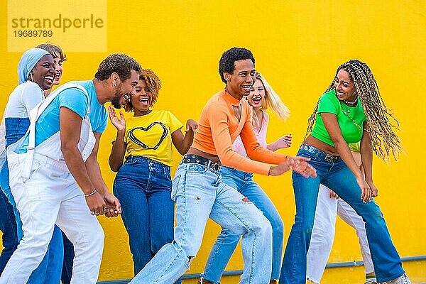 Multiethnische junge Freunde tanzen gemeinsam eine Choreografie auf der Straße vor einem gelben Hintergrund
