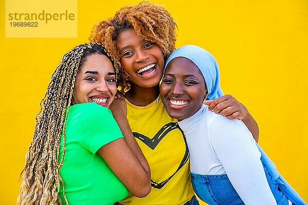 Nahaufnahme eines lächelnden multiethnischen Mädchens  das zusammen vor einem gelben Hintergrund posiert