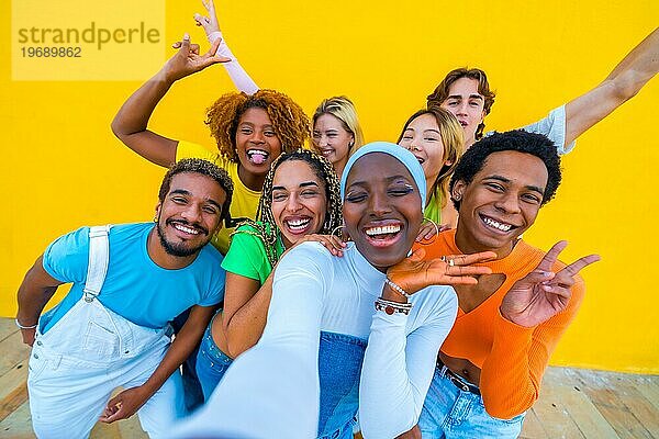 Frontalansicht einer multiethnischen Gruppe von Freunden  die fröhlich gestikulieren  während sie ein Selfie vor einem gelben Hintergrund machen