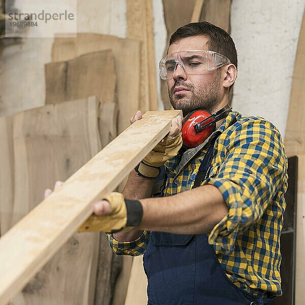 Männlicher Zimmermann  der ernsthaft nach einer Holzplanke sucht