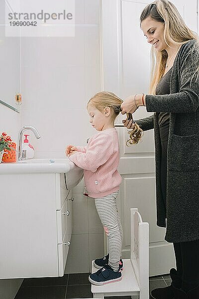 Glückliche Frau bindet ihrer Tochter die Haare