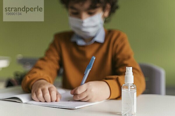 Frontansicht Kind mit medizinischer Maske Klasse mit Flasche Hand Desinfektionsmittel Schreibtisch