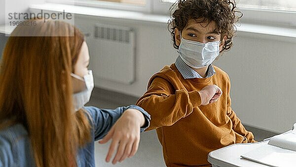 Kinder mit medizinischen Masken beim Ellbogengrußunterricht
