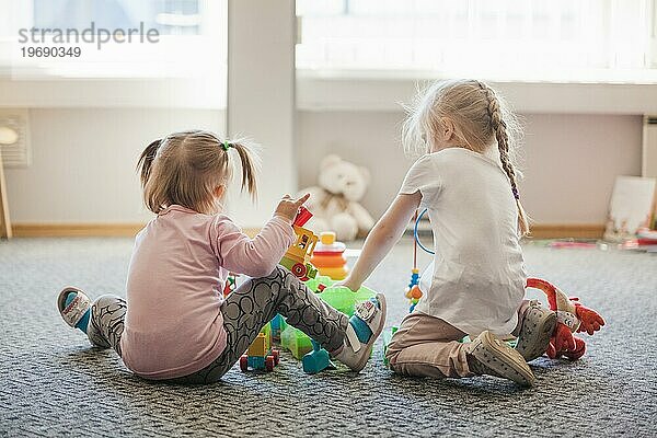 Zwei kleine Mädchen sitzen auf dem Boden und spielen