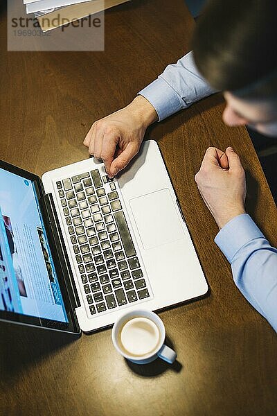 Von einem Mann  der in der Nähe einer Tasse Kaffee am Laptop sitzt