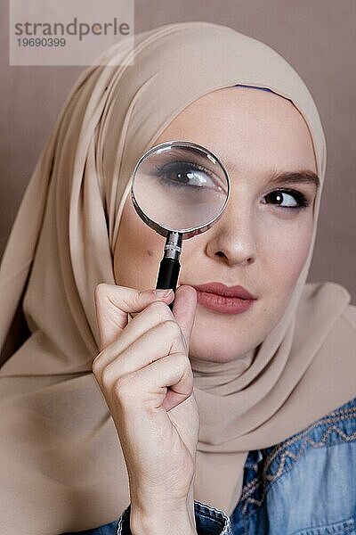 Nahaufnahme einer neugierigen muslimischen Frau  die durch ein Vergrößerungsglas schaut