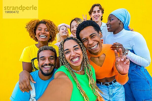 Gruppe verschiedener junger Menschen  die lächeln  während sie ein Selfie vor einem gelben Hintergrund machen