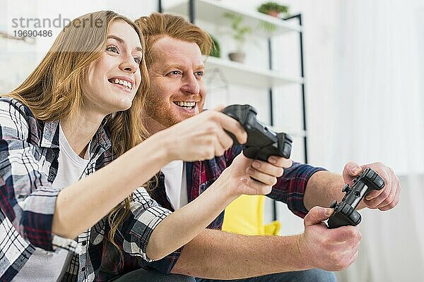 Glückliches Portrait eines jungen Paares beim Spielen einer Spielkonsole mit Joysticks