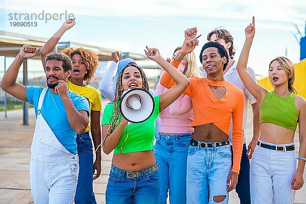 Geschlechtsunterschiedliche junge Menschen  die bei einem Protest auf einem städtischen Platz über einen Lautsprecher schreien
