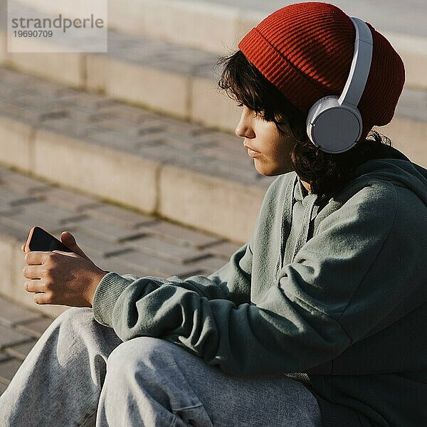 Teenager im Freien  der mit seinem Smartphone Musik über Kopfhörer hört