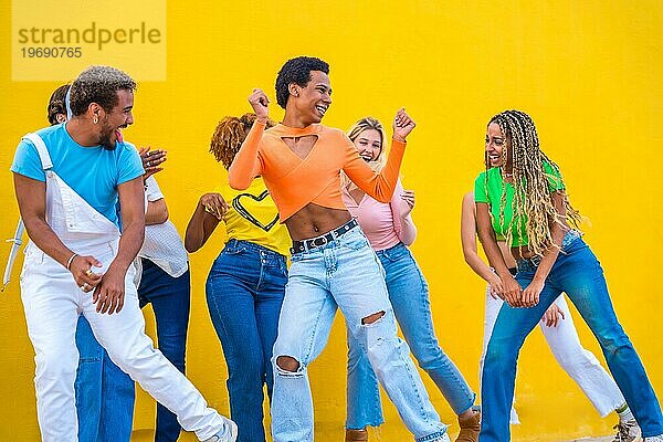 Junge Gruppe von Menschen tanzen zusammen in der Koordination auf der Straße neben einem gelben Hintergrund
