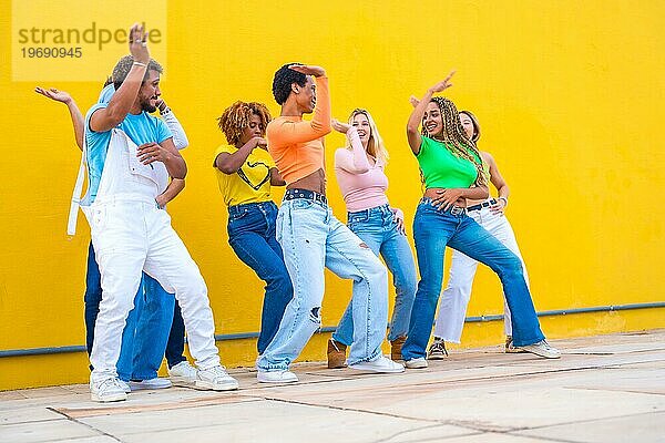 Eine Gruppe verschiedener ethnischer Gruppen tanzt eine gemeinsame Choreografie auf der Straße vor einem gelben städtischen Hintergrund