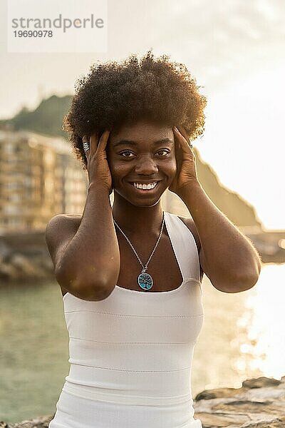 Vertikales Porträt einer glücklichen afrikanischen Frau  die neben dem Meer in die Kamera blickt
