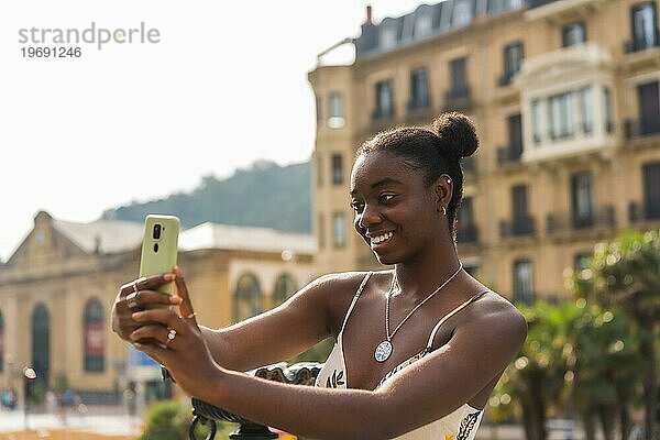 Seitenansicht einer süßen afrikanischen jungen Frau  die ein Selfie auf der Straße macht