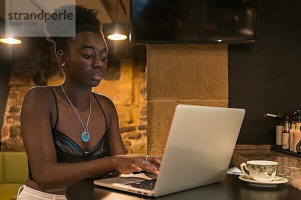 Konzentrierte junge Afrikanerin mit Laptop in einer Cafeteria