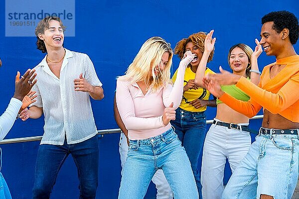 Blonde junge Frau tanzt in einer Tanzschlacht mit Freunden vor einer blauen Wand als Hintergrund