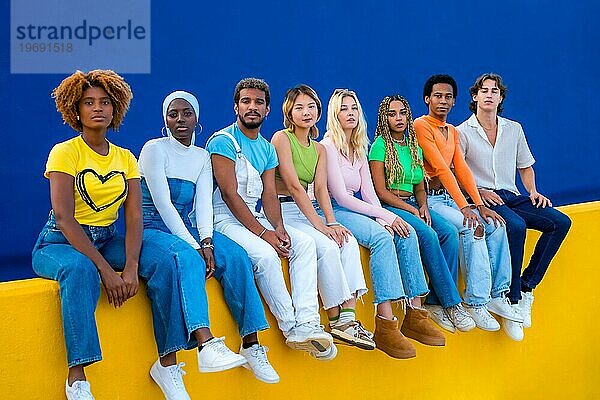 Seriöse Gruppe multiethnischer junger Menschen  die auf einer bunten Wand sitzen und in die Kamera schauen
