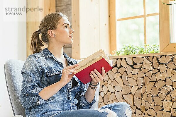 Attraktive junge Frau schaut zum Fenster und hält ein Buch