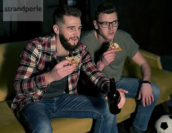 Männliche Freunde  die gemeinsam Sportfernsehen schauen und dabei Bierpizza essen