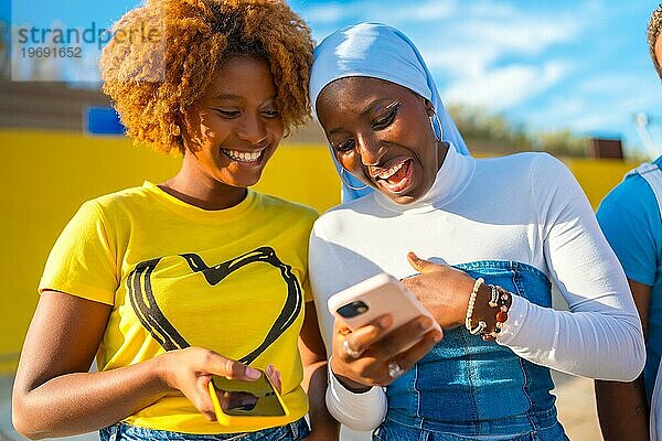 Frontalporträt einer muslimischen afrikanischen Frau und afroamerikanischen Freunden  die im Freien ein Mobiltelefon benutzen