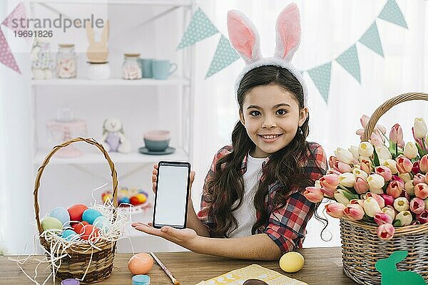 Glückliches Mädchen zeigt Handy mit Ostereiern Tulpen Korb Tisch