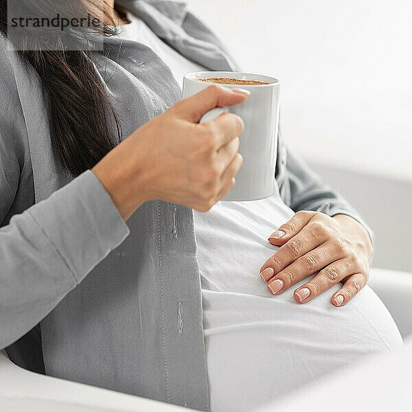 Seitenansicht schwangere Frau zu Hause hält Becher Kaffee