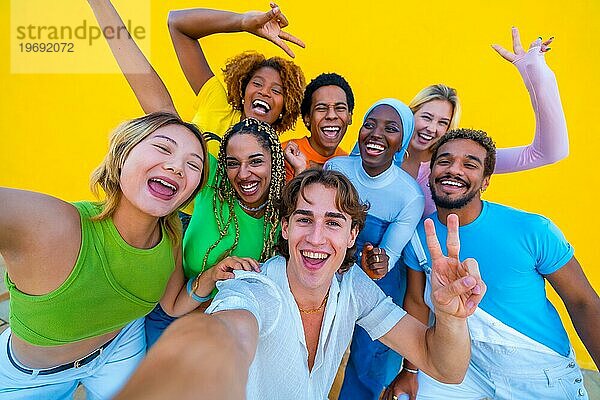 Junge Menschen verschiedener Ethnien machen ein fröhliches Selfie bei einer Versammlung vor einem gelben Hintergrund