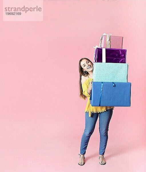 Glückliche Frau hält Stapel bunte Geschenkboxen gegen rosa Hintergrund