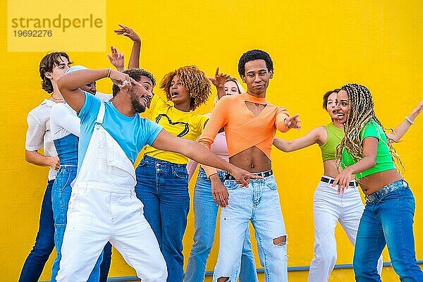 Multikulturelle Gruppe fröhlicher junger Menschen  die in einem gelben städtischen Raum zusammen tanzen