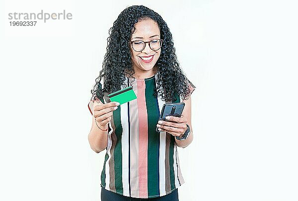 Lächelnde Afro Mädchen hält Kreditkarte Onlineshopping mit Telefon isoliert. Glückliche junge Frau macht Onlineeinkäufe mit Handys und Kreditkarten