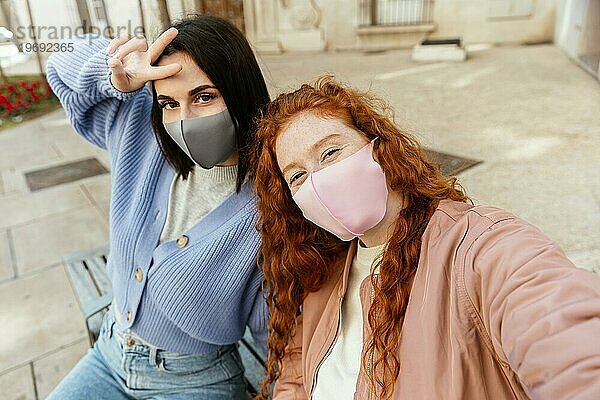 Zwei junge Freundinnen mit Gesichtsmasken im Freien nehmen Selfie