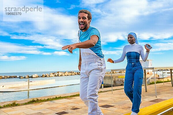 Seitenansicht von zwei glücklichen multiethnischen Freunden  die am Meer tanzen