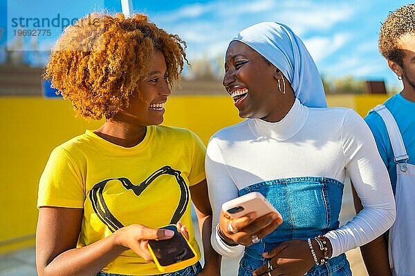 Frontal glücklich Porträt von zwei jungen afrikanischen amerikanischen jungen Frauen mit Telefon im Freien