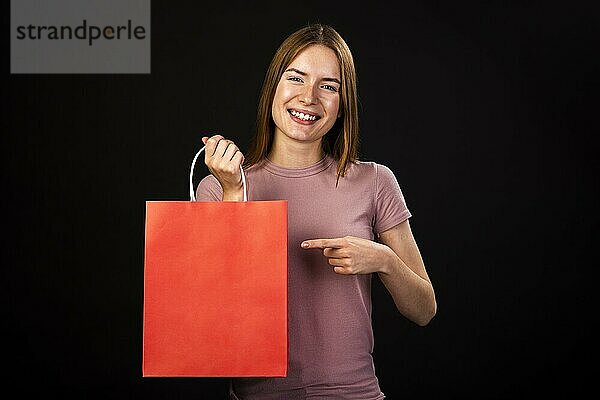 Vorderansicht glückliche Frau  die auf ihre rote Einkaufstasche zeigt