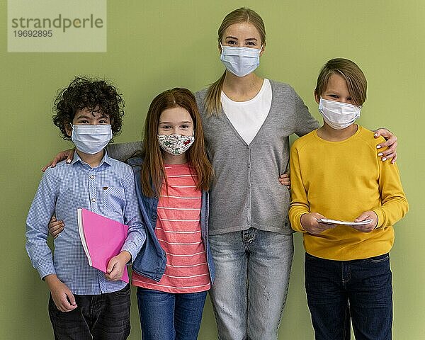 Lehrerin mit medizinischer Maske posiert mit Kindern in der Schule