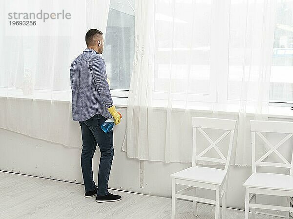 Seitenansicht Mann schaut beim Putzen durch das Fenster