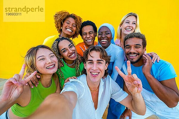 Multiethnische Freunde gestikulieren erfolgreich  während sie ein Selfie neben einer gelben Wand machen