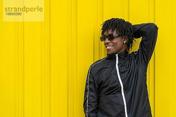 Cooler junger afrikanischer Mann posiert entspannt im Freien neben einem städtischen gelben Hintergrund