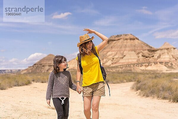 Horizontale Frontalansicht einer Mutter und eines Mädchens  die sich an den Händen halten und in einem trockenen Nationalpark spazieren gehen