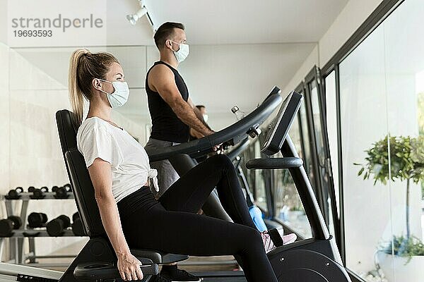 Seitenansicht Frau Mann Fitnessstudio mit medizinischen Masken