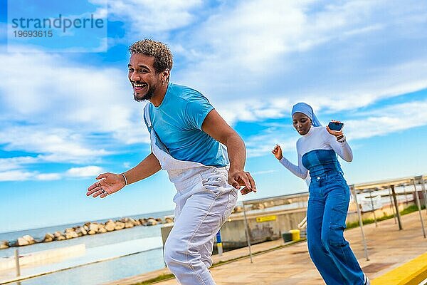 Muslimische Frau und gemischtrassiger Mann tanzen Freestyle auf der Straße am Meer