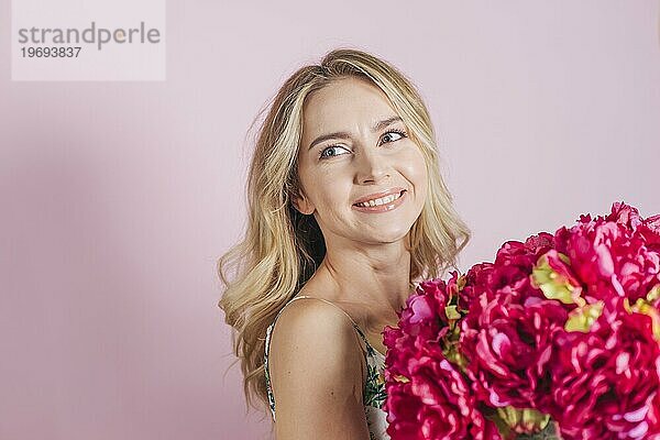 Schöne junge Frau hält Rosenstrauß gegen rosa Hintergrund