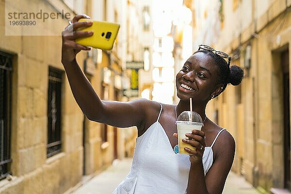 Glückliche junge afroamerikanische Frau  die ein Selfie mit einem leckeren Milchshake auf der Straße in der Stadt macht