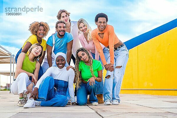 Multiethnische junge Menschen posieren im Freien und lächeln zusammen neben einem bunten Hintergrund